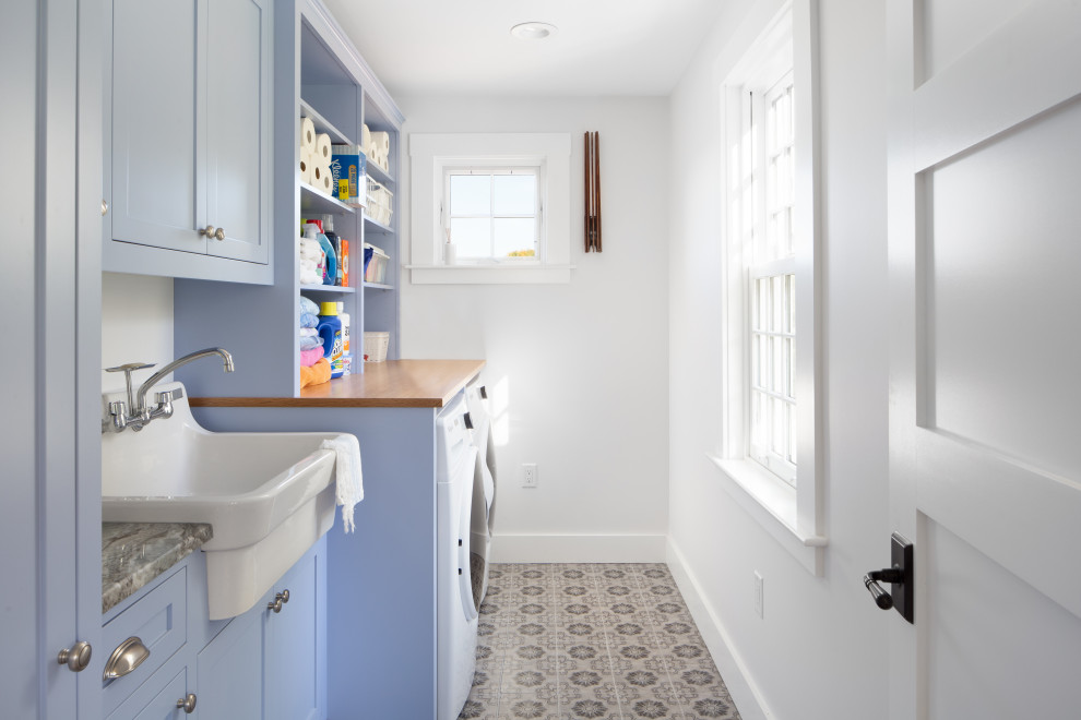Inspiration for a mid-sized transitional single-wall dedicated laundry room in Providence with a farmhouse sink, shaker cabinets, blue cabinets, wood benchtops, white walls, ceramic floors, a side-by-side washer and dryer, grey floor and beige benchtop.