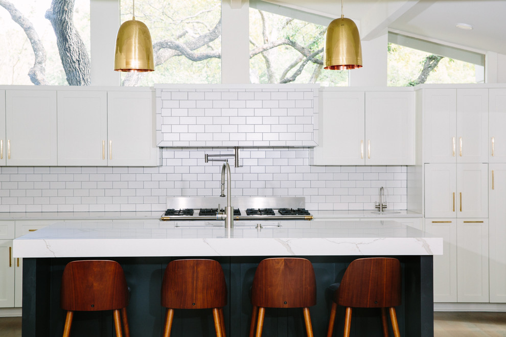 Southill - We completely gutted the client's existing kitchen and opened up the space.  We kept the windows bare to let in beautiful light and showcase the oak trees outside, used oversized unlacquered brass cabinet hardware, and painted the island a dark to contrast against the light tile, cabinetry and countertops.