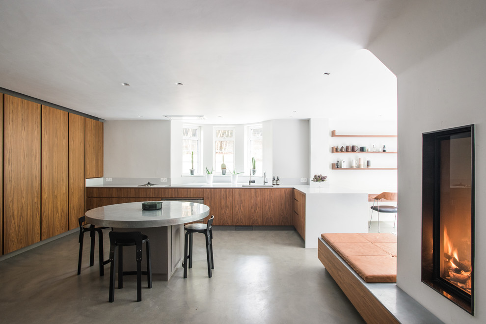 Photo of a modern u-shaped eat-in kitchen in London with an undermount sink, flat-panel cabinets, medium wood cabinets, panelled appliances, concrete floors, a peninsula, grey floor and white benchtop.