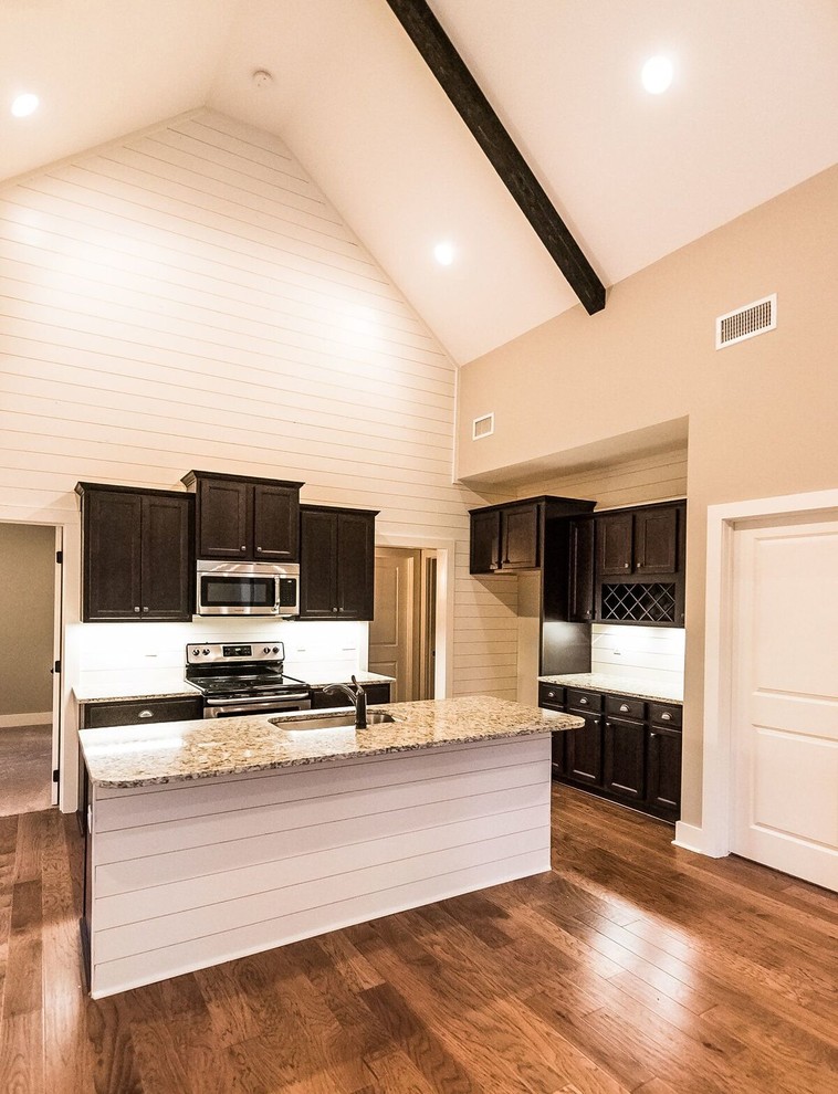 Photo of a large traditional u-shaped eat-in kitchen in Atlanta with an undermount sink, raised-panel cabinets, black cabinets, granite benchtops, white splashback, timber splashback, stainless steel appliances, dark hardwood floors, with island, brown floor and multi-coloured benchtop.