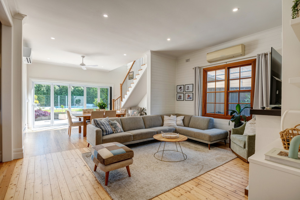 Design ideas for a transitional open concept living room in Sydney with white walls, light hardwood floors, a wall-mounted tv, beige floor and planked wall panelling.