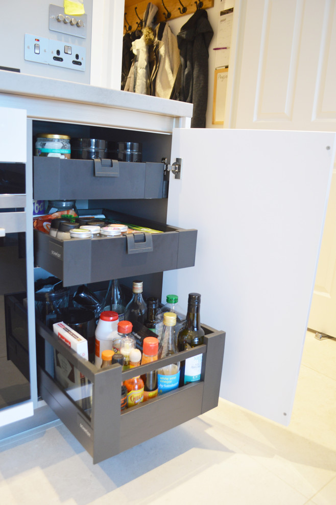 Medium sized contemporary l-shaped kitchen/diner in London with a built-in sink, beaded cabinets, white cabinets, laminate countertops, blue splashback, glass tiled splashback, black appliances and no island.