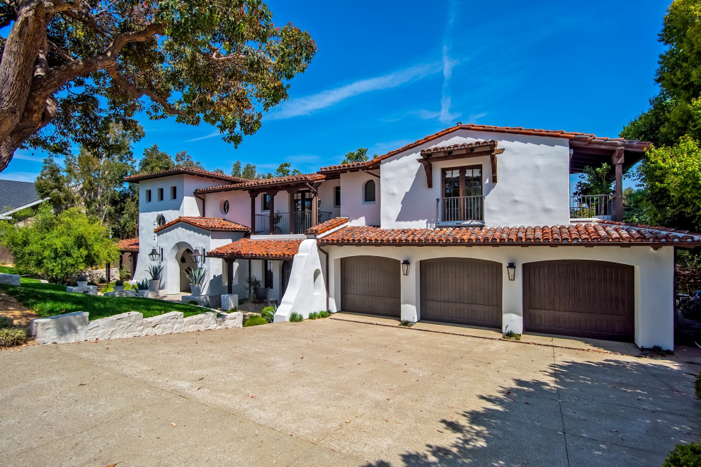 This is an example of a mediterranean two-storey white house exterior in Orange County with a gable roof and a tile roof.