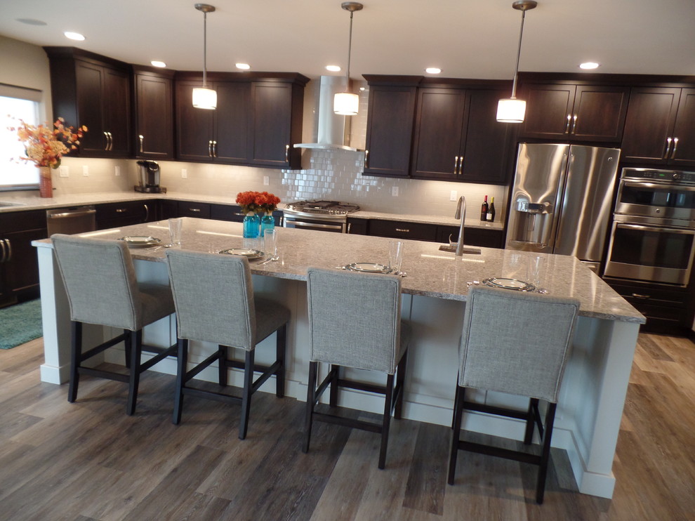 Inspiration for a large transitional l-shaped medium tone wood floor and beige floor eat-in kitchen remodel in Cedar Rapids with an undermount sink, shaker cabinets, dark wood cabinets, granite countertops, white backsplash, subway tile backsplash, stainless steel appliances and an island