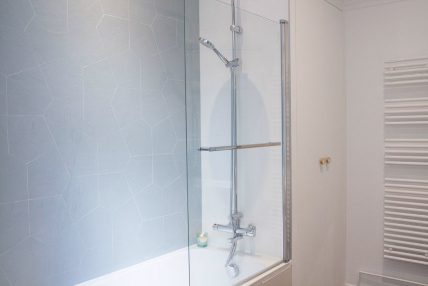 Aménagement de salle de bain en bois clair avec une baignoire encastrée, parquet foncé, un lavabo posé, un plan de toilette en terrazzo et un plan de toilette blanc.