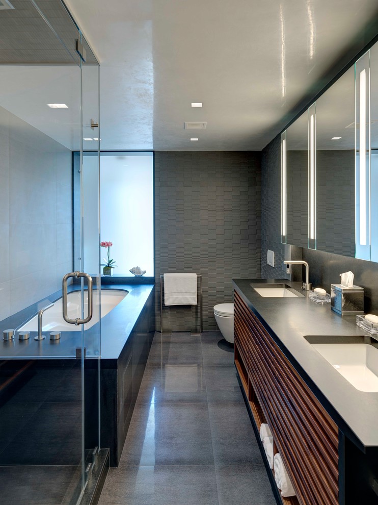 Mid-sized modern master bathroom in New York with dark wood cabinets, a drop-in tub, a wall-mount toilet, gray tile, cement tile, grey walls, concrete floors, an undermount sink, marble benchtops and grey floor.