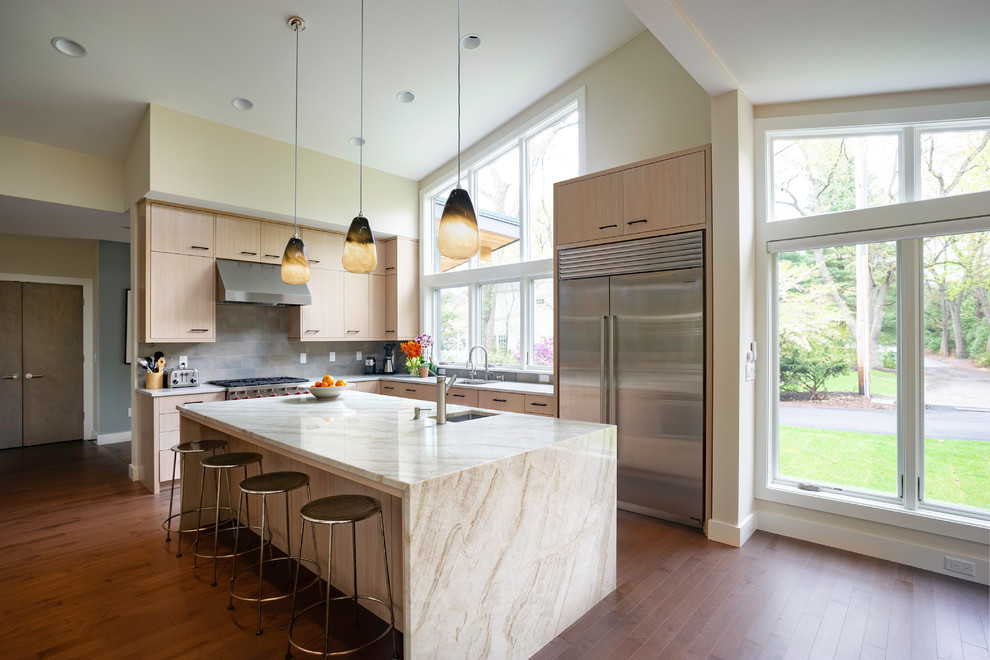 Contemporary l-shaped kitchen in Boston with an undermount sink, flat-panel cabinets, light wood cabinets, grey splashback, stainless steel appliances, medium hardwood floors, with island and grey benchtop.