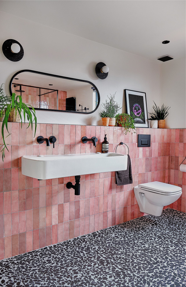 Inspiration for a mid-sized contemporary kids bathroom in London with black cabinets, an open shower, a wall-mount toilet, pink tile, ceramic tile, white walls, terrazzo floors, a trough sink, black floor, an open shower, a niche and a single vanity.