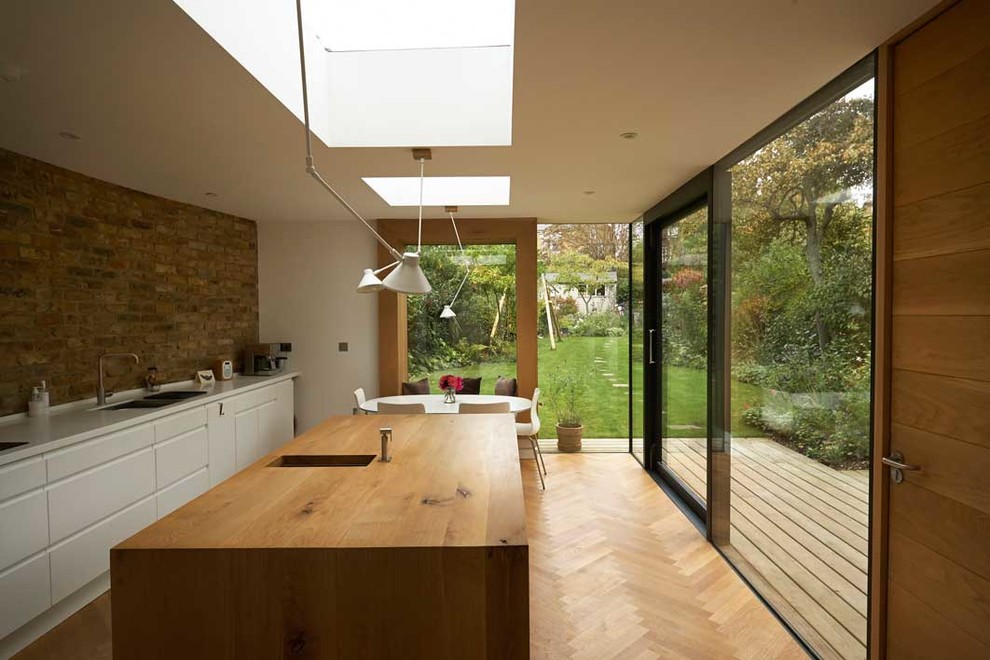 Mid-sized contemporary single-wall separate kitchen in London with a double-bowl sink, flat-panel cabinets, white cabinets, wood benchtops, light hardwood floors, with island and beige floor.