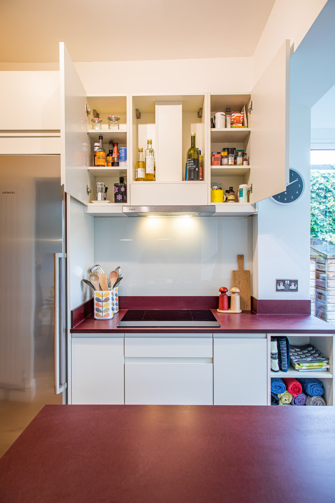 This is an example of a small contemporary u-shaped kitchen/diner in Other with flat-panel cabinets, white cabinets, white splashback, glass sheet splashback, stainless steel appliances, no island, brown floors and red worktops.