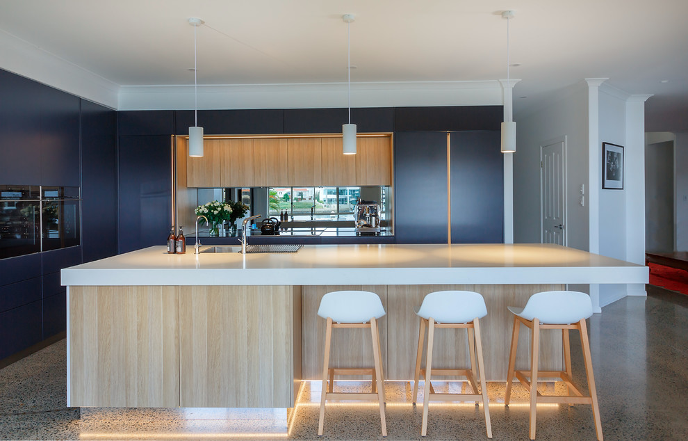 Inspiration for a large contemporary l-shaped kitchen pantry in Brisbane with a double-bowl sink, flat-panel cabinets, light wood cabinets, quartz benchtops, mirror splashback, black appliances, concrete floors, with island, multi-coloured floor and white benchtop.