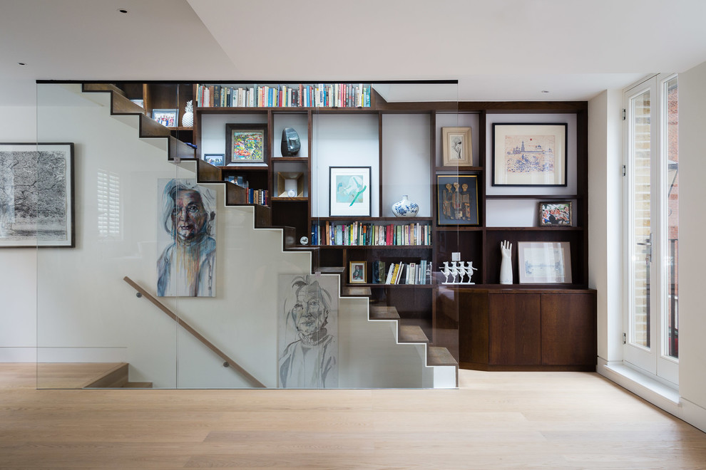 This is an example of a transitional wood straight staircase in London with wood risers and glass railing.