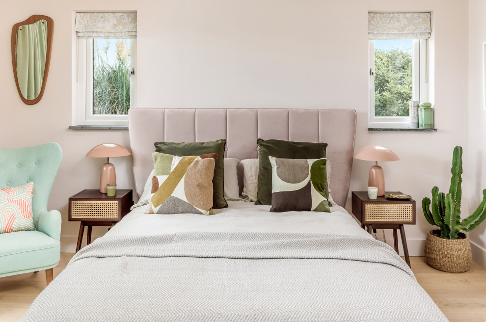 Photo of a large midcentury guest bedroom in London with pink walls and light hardwood floors.