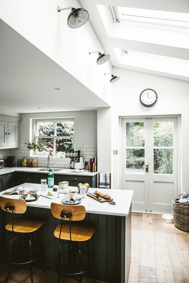 This is an example of a contemporary eat-in kitchen in London with an undermount sink, shaker cabinets, grey cabinets, marble benchtops, ceramic splashback, medium hardwood floors and with island.