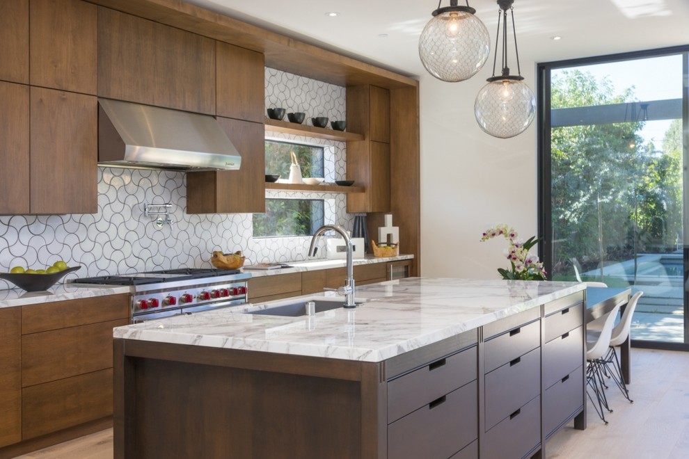 This is an example of a contemporary galley kitchen in San Francisco with an undermount sink, flat-panel cabinets, dark wood cabinets, marble benchtops, white splashback, ceramic splashback, stainless steel appliances, light hardwood floors and with island.
