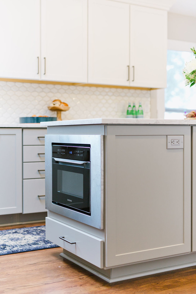 Example of a mid-sized transitional u-shaped medium tone wood floor and brown floor open concept kitchen design with an undermount sink, shaker cabinets, white cabinets, quartz countertops, white backsplash, porcelain backsplash, stainless steel appliances, an island and white countertops