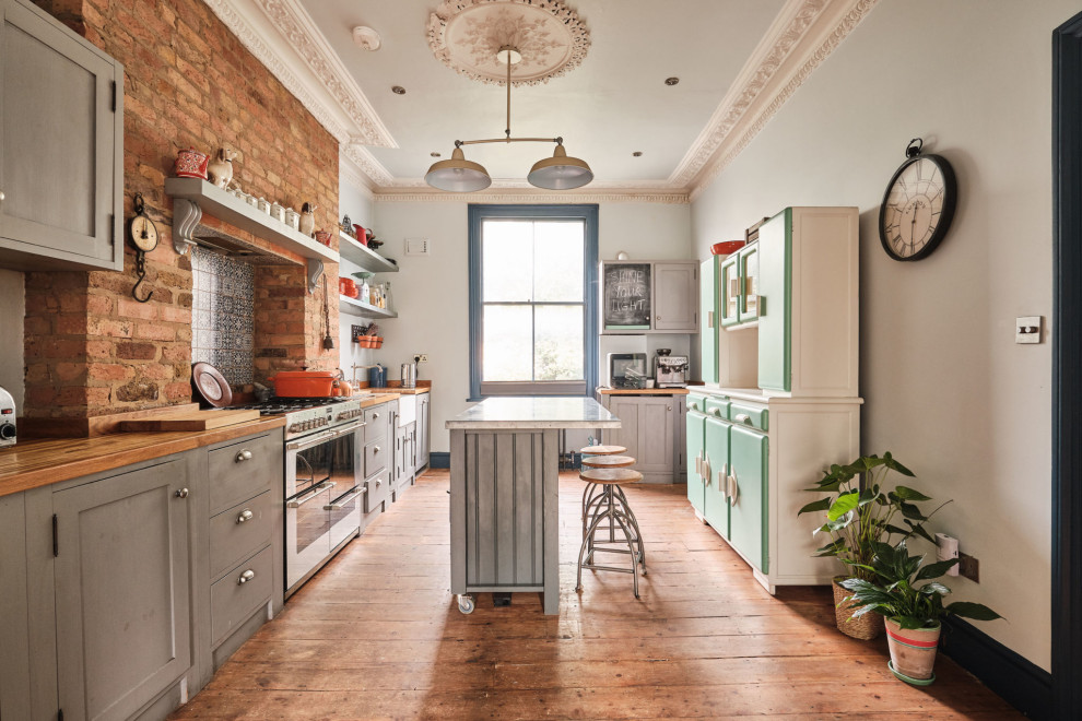 Photo of a large eclectic galley open plan kitchen in London with a farmhouse sink, shaker cabinets, grey cabinets, zinc benchtops, blue splashback, ceramic splashback, coloured appliances, medium hardwood floors, with island and grey benchtop.