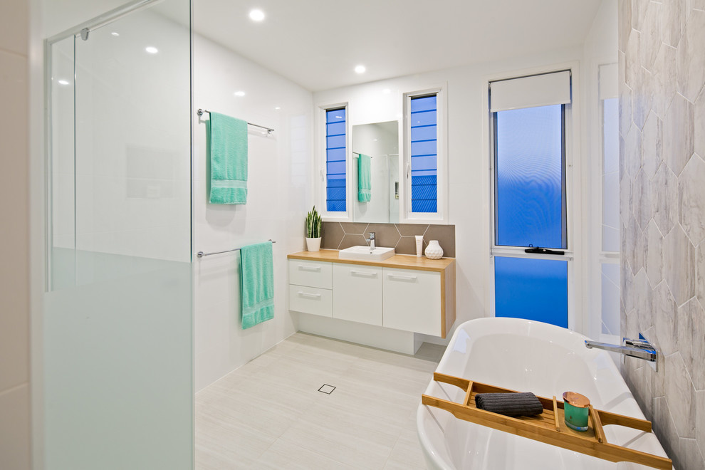 Photo of a large scandinavian kids bathroom in Brisbane with a freestanding tub, a double shower, a one-piece toilet, porcelain tile, white walls, porcelain floors, a drop-in sink, beige floor, a hinged shower door, white cabinets, multi-coloured tile and laminate benchtops.
