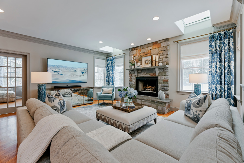 Inspiration for a transitional open concept family room in Philadelphia with white walls, medium hardwood floors, a standard fireplace, a stone fireplace surround, a wall-mounted tv and brown floor.