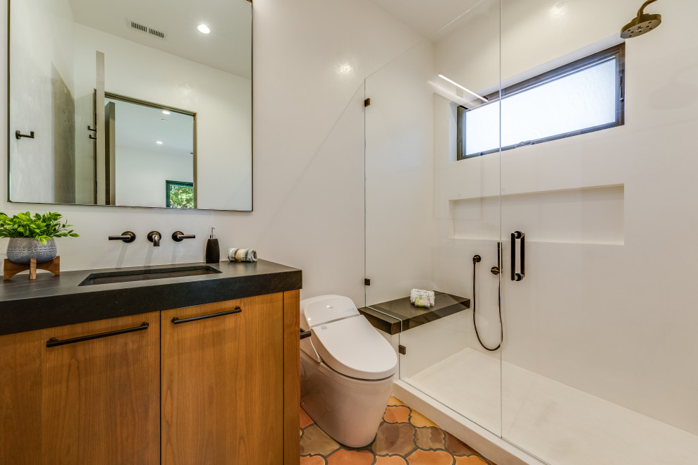 This is an example of a mid-sized mediterranean bathroom in San Francisco with flat-panel cabinets, brown cabinets, a double shower, a one-piece toilet, white tile, white walls, terra-cotta floors, an undermount sink, quartzite benchtops, red floor, black benchtops, a niche, a single vanity and a built-in vanity.
