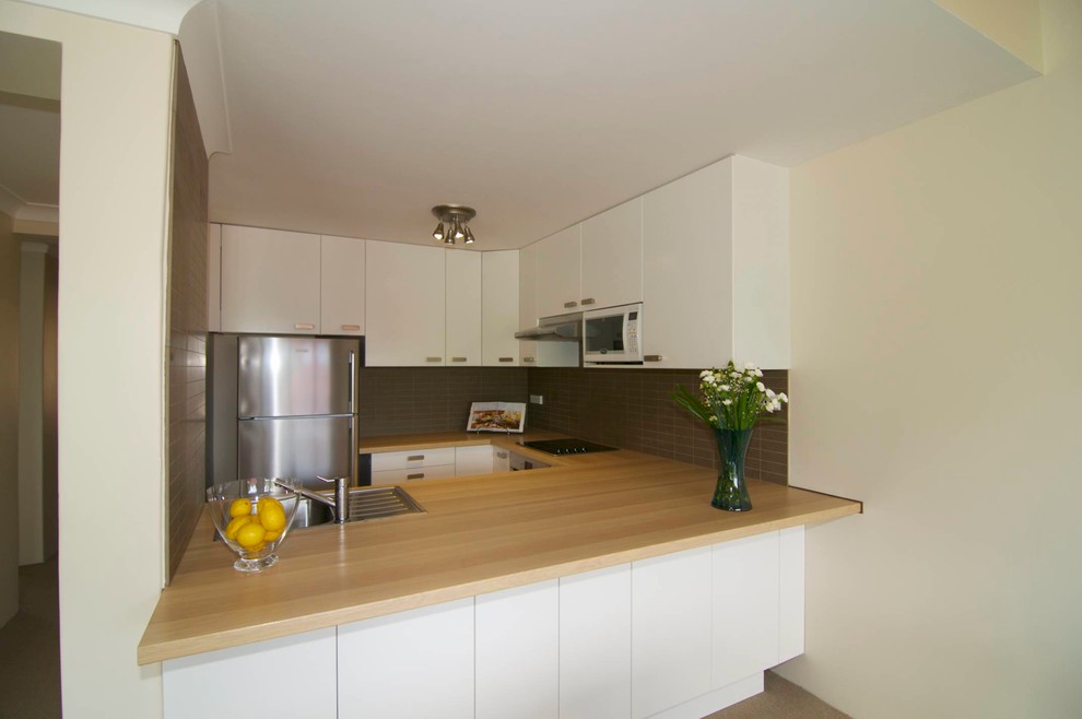 Design ideas for a small modern u-shaped eat-in kitchen in Perth with a drop-in sink, flat-panel cabinets, white cabinets, wood benchtops, brown splashback, ceramic splashback, stainless steel appliances, linoleum floors and no island.