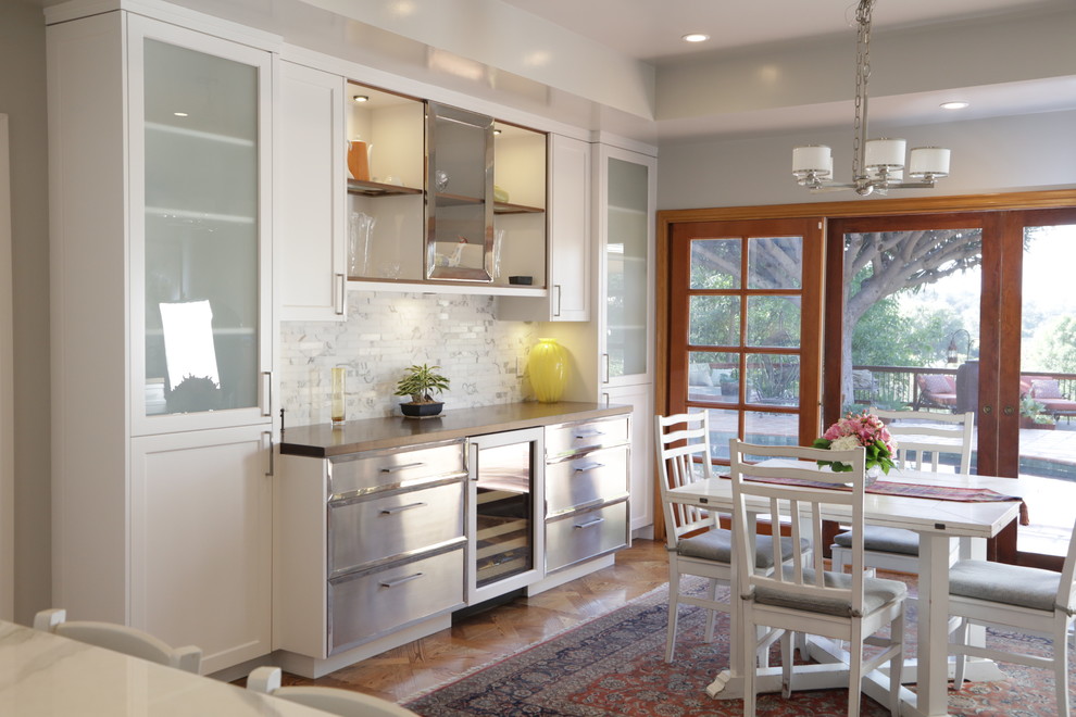 Eat-in kitchen - large transitional u-shaped medium tone wood floor eat-in kitchen idea in Los Angeles with an undermount sink, recessed-panel cabinets, white cabinets, wood countertops, white backsplash, stone tile backsplash, stainless steel appliances and an island
