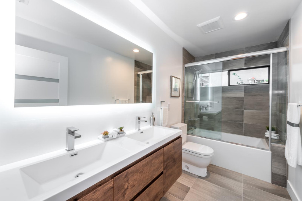 Design ideas for a mid-sized transitional bathroom in Orange County with white cabinets, a shower/bathtub combo, a one-piece toilet, white tile, wood-look tile, white walls, porcelain floors, a drop-in sink, solid surface benchtops, brown floor, a sliding shower screen, white benchtops, a double vanity, a floating vanity and exposed beam.