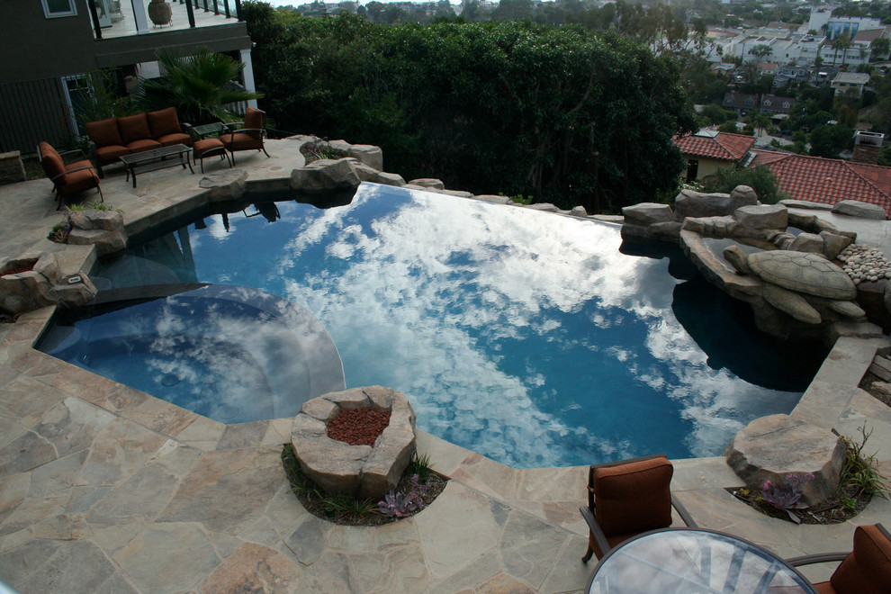This is an example of a large contemporary backyard custom-shaped infinity pool in Orange County with a hot tub and natural stone pavers.