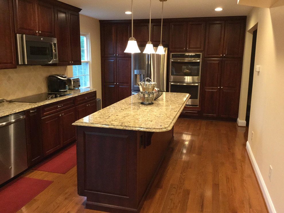 Inspiration for a transitional medium tone wood floor kitchen remodel in Baltimore with an undermount sink, raised-panel cabinets, dark wood cabinets, quartz countertops, beige backsplash, stone tile backsplash, stainless steel appliances and an island