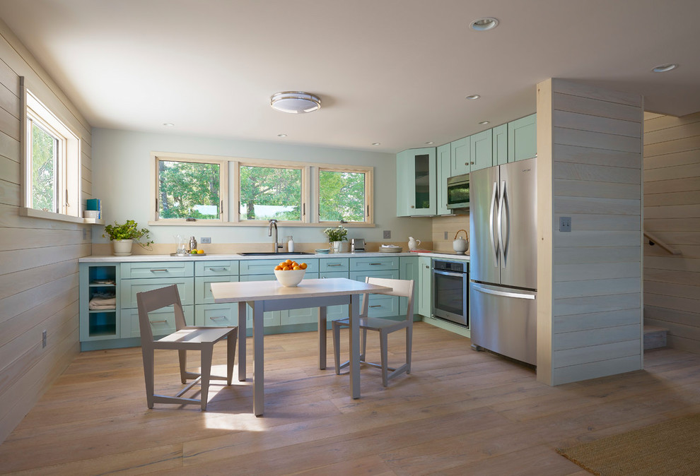 Inspiration for a mid-sized beach style l-shaped eat-in kitchen in Portland Maine with shaker cabinets, beige splashback, timber splashback, stainless steel appliances, light hardwood floors, no island, brown floor, a drop-in sink, laminate benchtops and turquoise cabinets.