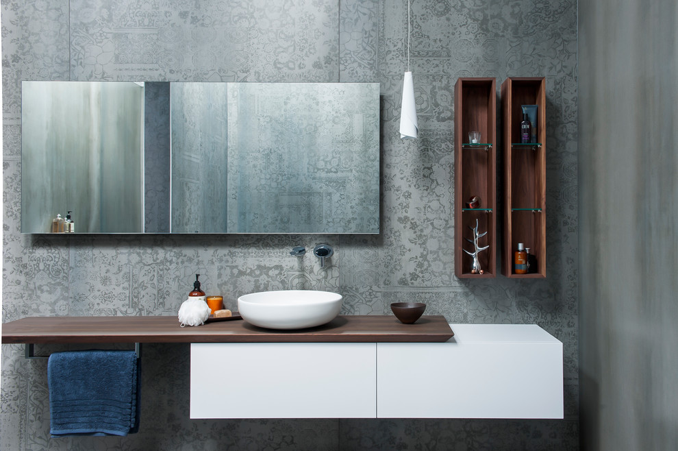 This is an example of a large contemporary master bathroom in Sydney with a vessel sink, furniture-like cabinets, medium wood cabinets, wood benchtops, a freestanding tub, an open shower, a one-piece toilet, gray tile, ceramic tile, grey walls and ceramic floors.