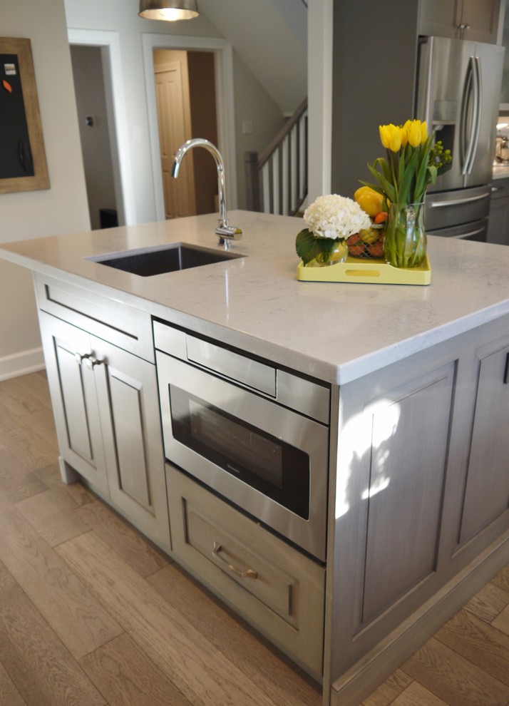 Enclosed kitchen - mid-sized transitional l-shaped light wood floor enclosed kitchen idea in Toronto with an undermount sink, recessed-panel cabinets, gray cabinets, quartz countertops, white backsplash, porcelain backsplash, stainless steel appliances and an island