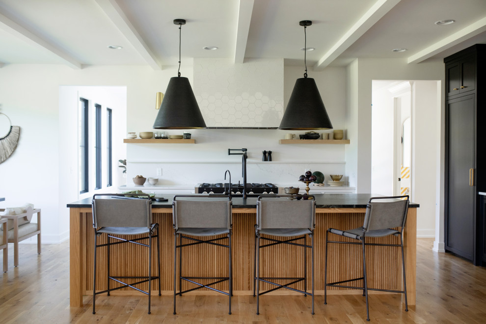Transitional u-shaped medium tone wood floor, brown floor and exposed beam eat-in kitchen photo in Grand Rapids with an undermount sink, shaker cabinets, black cabinets, quartz countertops, white backsplash, paneled appliances, an island and black countertops