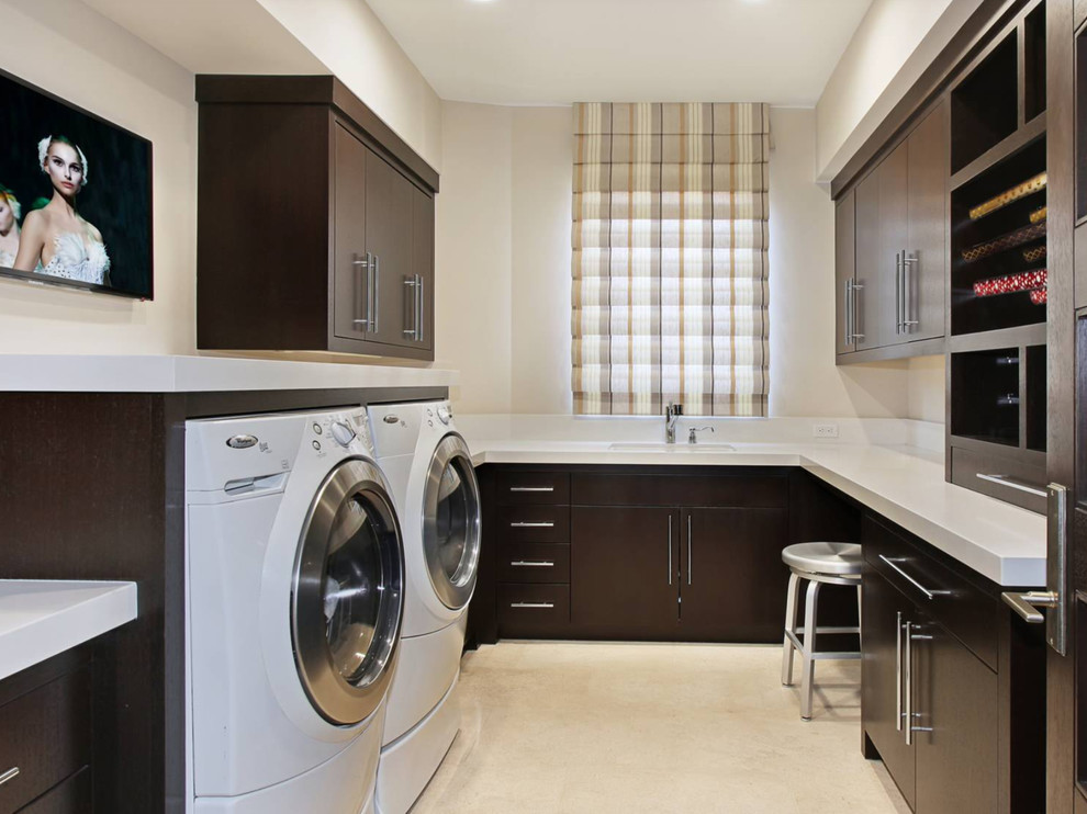 This is an example of a large contemporary l-shaped utility room in Other with an integrated sink, flat-panel cabinets, dark wood cabinets, beige walls and a side-by-side washer and dryer.