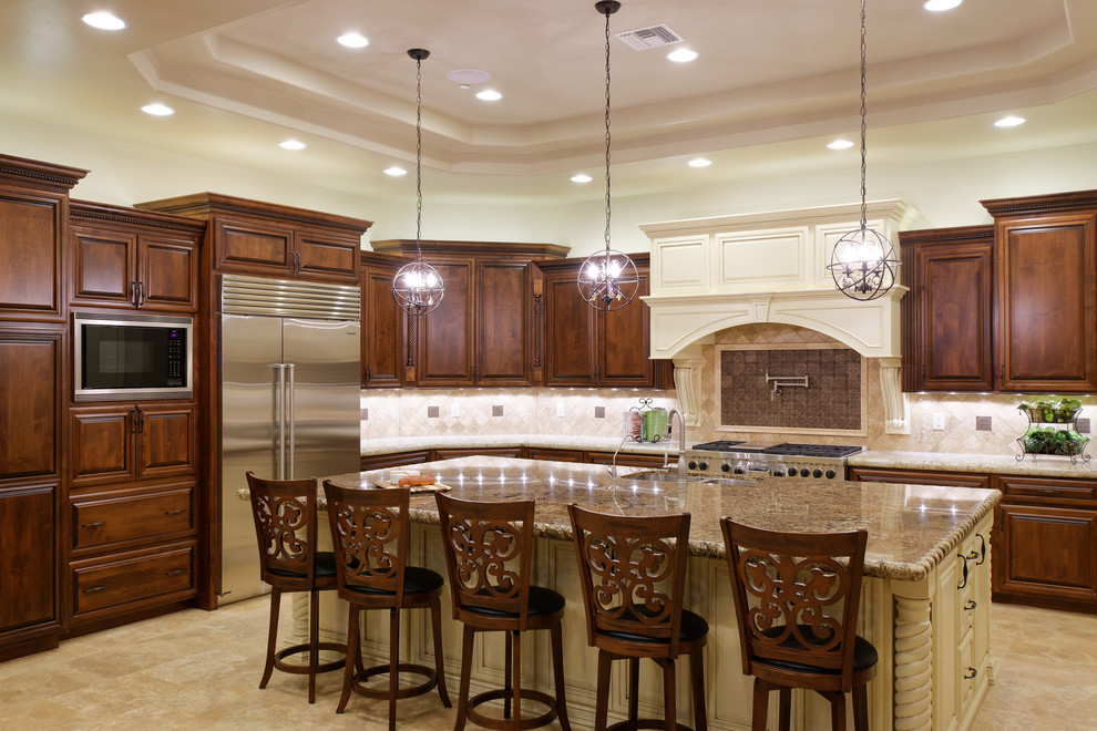 Photo of a mediterranean kitchen in Phoenix with raised-panel cabinets, dark wood cabinets, granite benchtops, stainless steel appliances, travertine floors, with island and porcelain splashback.