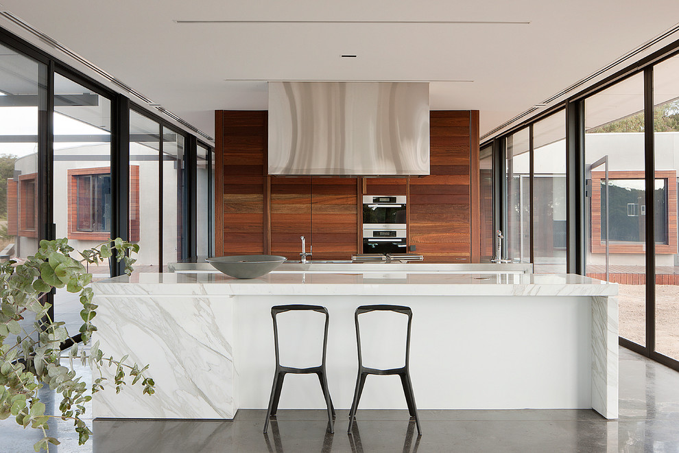 This is an example of a mid-sized contemporary galley kitchen in Melbourne with flat-panel cabinets, marble benchtops, stainless steel appliances and with island.