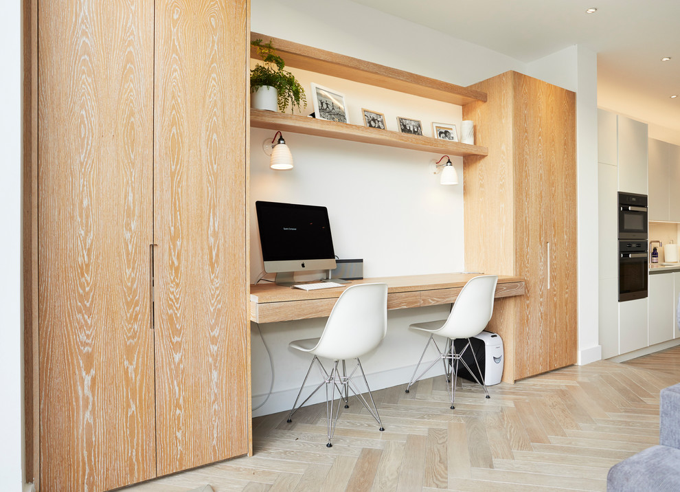 This is an example of a small contemporary home office in London with white walls, light hardwood floors, a built-in desk and beige floor.