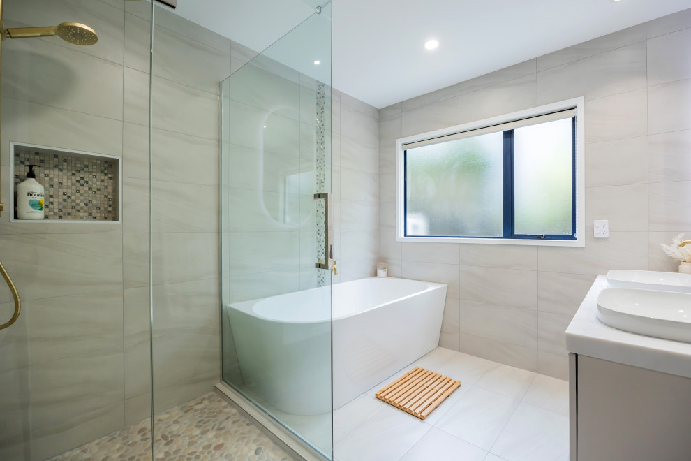 Medium sized modern family bathroom in Auckland with shaker cabinets, white cabinets, a corner bath, a corner shower, grey tiles, porcelain tiles, grey walls, porcelain flooring, a vessel sink, engineered stone worktops, grey floors, a hinged door, white worktops, a wall niche, double sinks and a floating vanity unit.