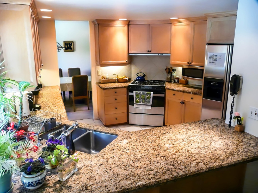 Example of a mid-sized transitional l-shaped porcelain tile enclosed kitchen design in San Diego with an undermount sink, recessed-panel cabinets, light wood cabinets, granite countertops, beige backsplash, porcelain backsplash, stainless steel appliances and no island