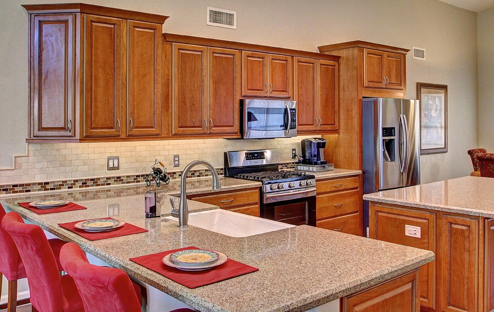 Inspiration for a mid-sized l-shaped medium tone wood floor eat-in kitchen remodel in Phoenix with a farmhouse sink, raised-panel cabinets, medium tone wood cabinets, beige backsplash, stone tile backsplash, stainless steel appliances and an island