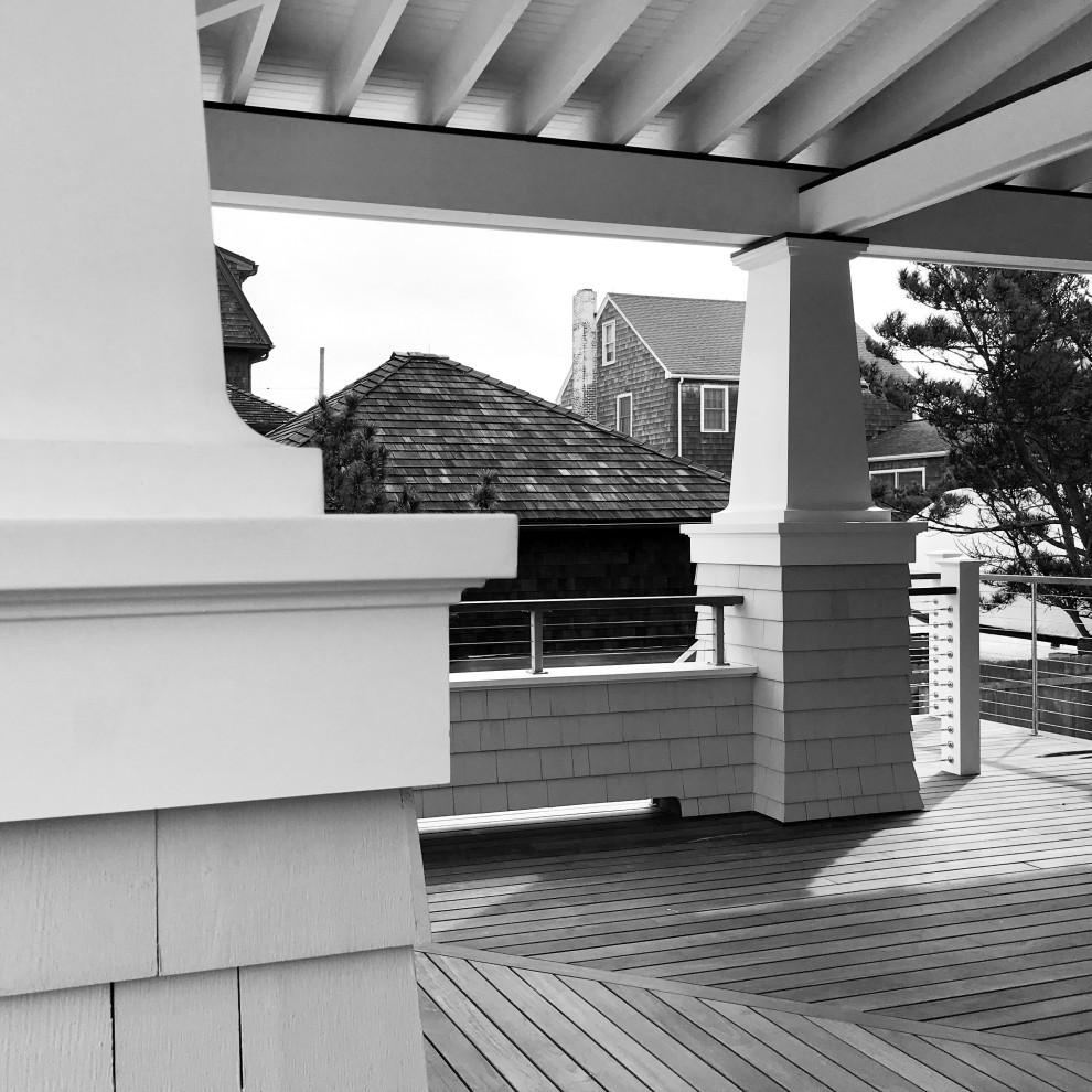 Photo of a large beach style front yard verandah in New York with decking, a roof extension, with columns and cable railing.