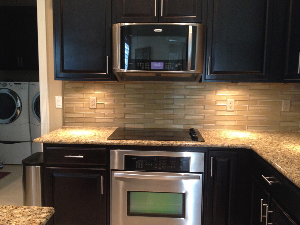 Kitchen - contemporary porcelain tile kitchen idea with dark wood cabinets, granite countertops, beige backsplash, glass tile backsplash and stainless steel appliances