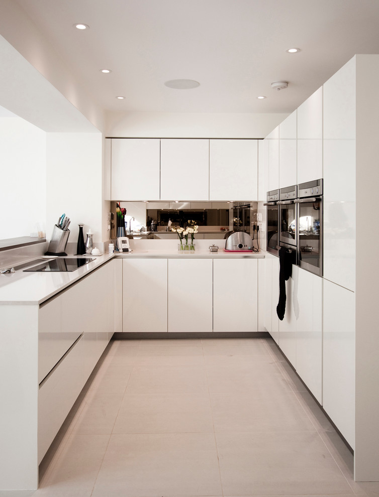 Contemporary u-shaped separate kitchen in Berkshire with flat-panel cabinets, white cabinets, metallic splashback and stainless steel appliances.