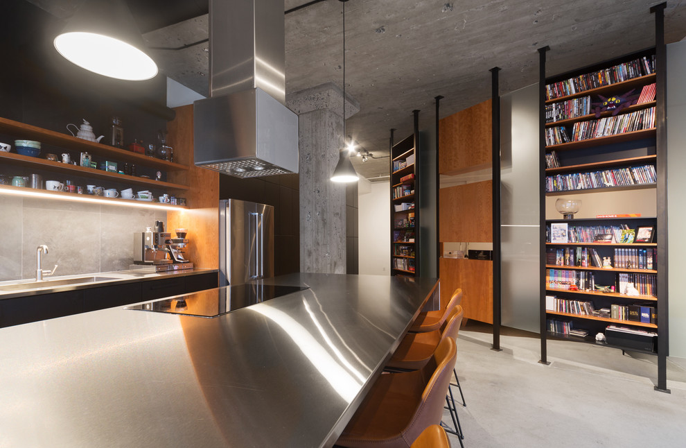 This is an example of a mid-sized industrial galley eat-in kitchen in Montreal with a drop-in sink, flat-panel cabinets, black cabinets, stainless steel benchtops, grey splashback, slate splashback, stainless steel appliances, slate floors, with island, grey floor and grey benchtop.
