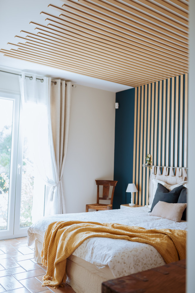 Idée de décoration pour une chambre parentale champêtre de taille moyenne avec un mur bleu, tomettes au sol et boiseries.
