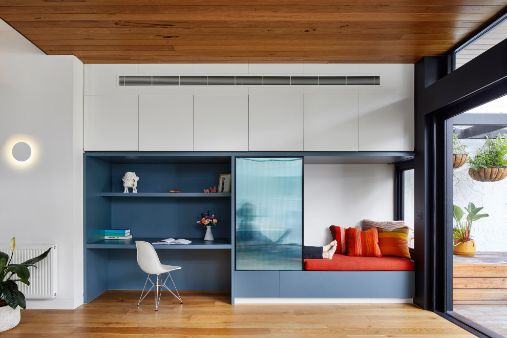 Modelo de despacho contemporáneo de tamaño medio con paredes azules, suelo de madera clara, escritorio empotrado, suelo beige y madera