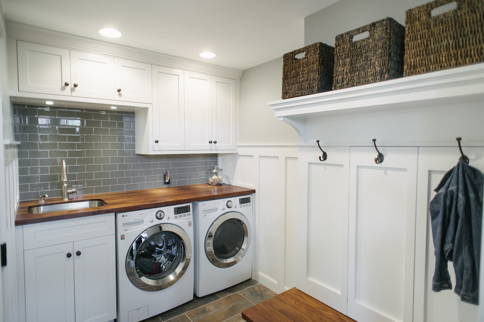 This is an example of a mid-sized arts and crafts l-shaped utility room in Detroit with an undermount sink, white cabinets, wood benchtops, grey walls, porcelain floors, a side-by-side washer and dryer, brown benchtop and shaker cabinets.