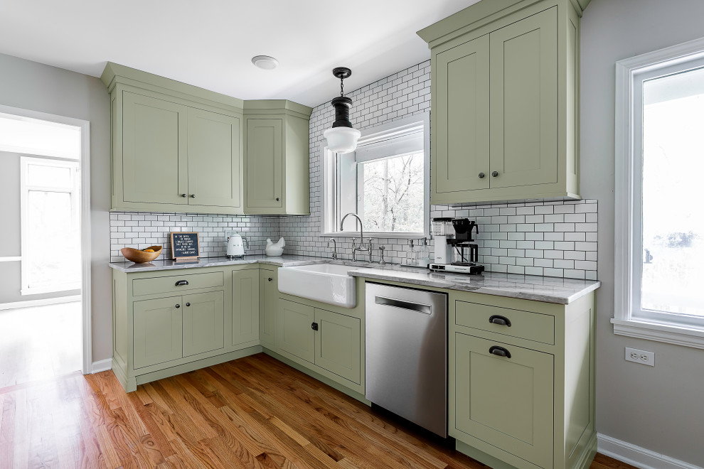 This is an example of a mid-sized country l-shaped eat-in kitchen in Other with a farmhouse sink, shaker cabinets, green cabinets, marble benchtops, white splashback, subway tile splashback, stainless steel appliances, medium hardwood floors, with island, multi-coloured floor and grey benchtop.