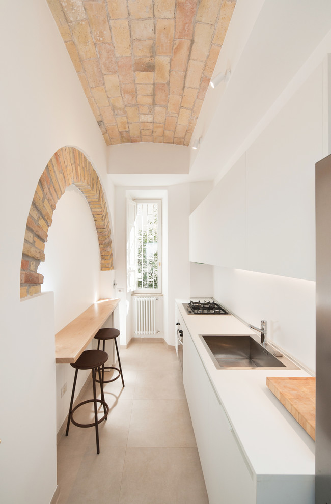 This is an example of a mediterranean galley kitchen in Rome with porcelain floors, flat-panel cabinets, white cabinets, white splashback, stainless steel appliances, white benchtop, a drop-in sink, no island and beige floor.