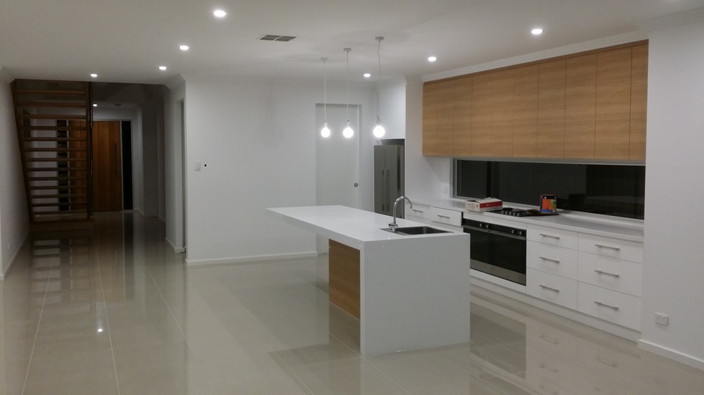 Large modern galley open plan kitchen in Adelaide with a single-bowl sink, flat-panel cabinets, white cabinets, quartz benchtops, white splashback, stainless steel appliances, ceramic floors and with island.